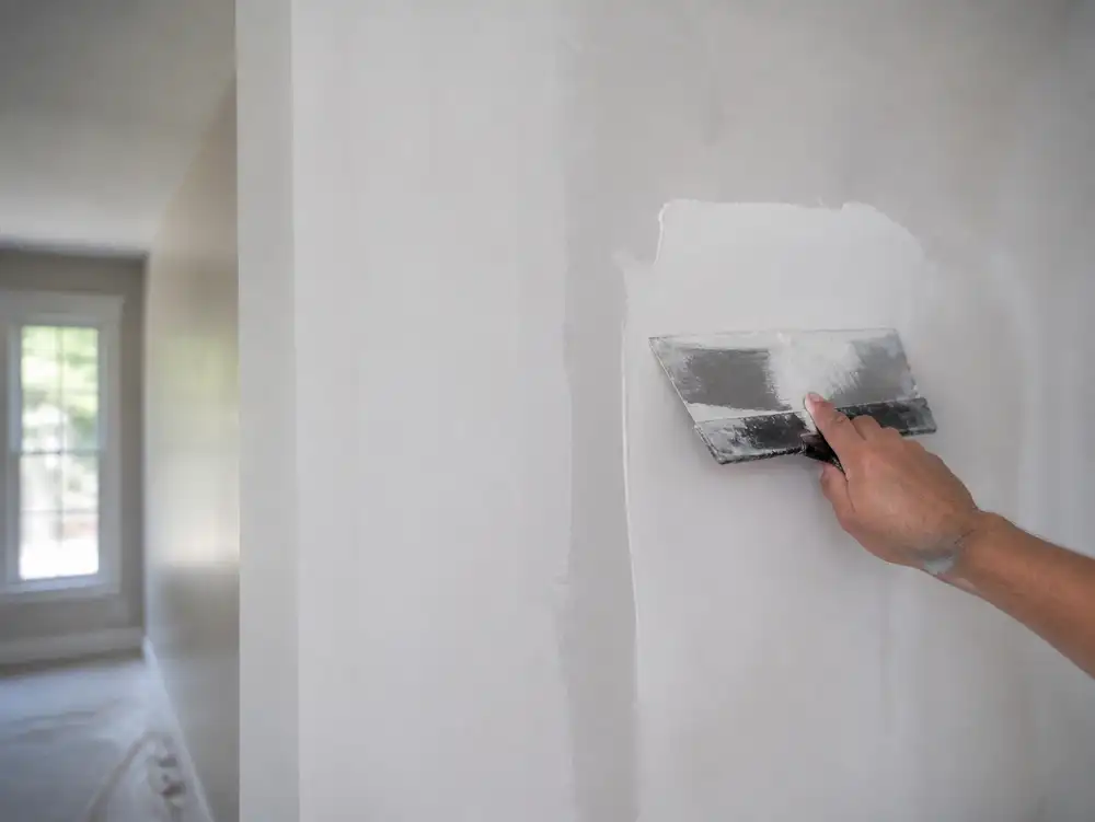 A person is using a handheld sander to remove paint from a wall.
